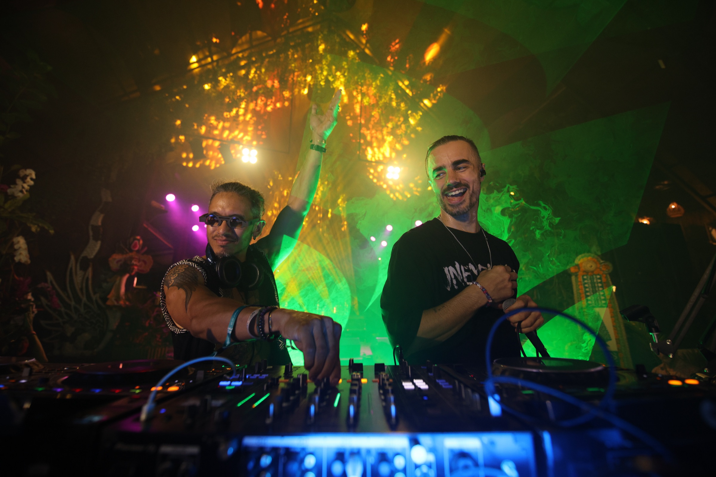 Miguel laughing reaching for the decks while Shalman leans with arm raised at Bali Spirit Festival 2026