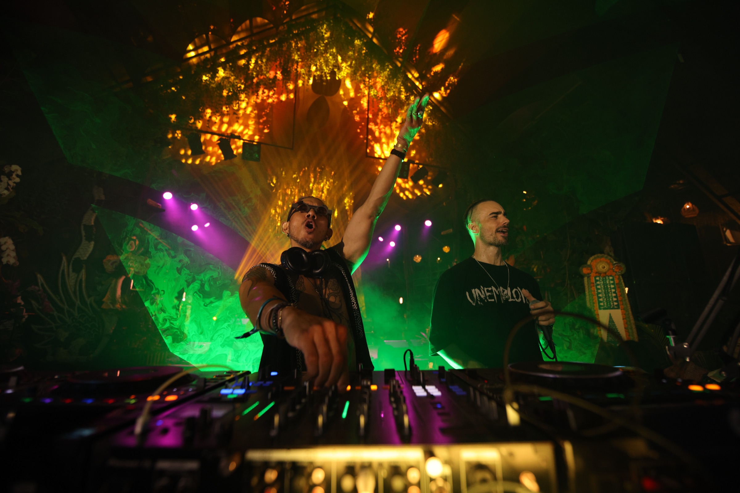 Shalman with arm raised high and Miguel behind, low angle, golden green light at Bali Spirit Festival 2026