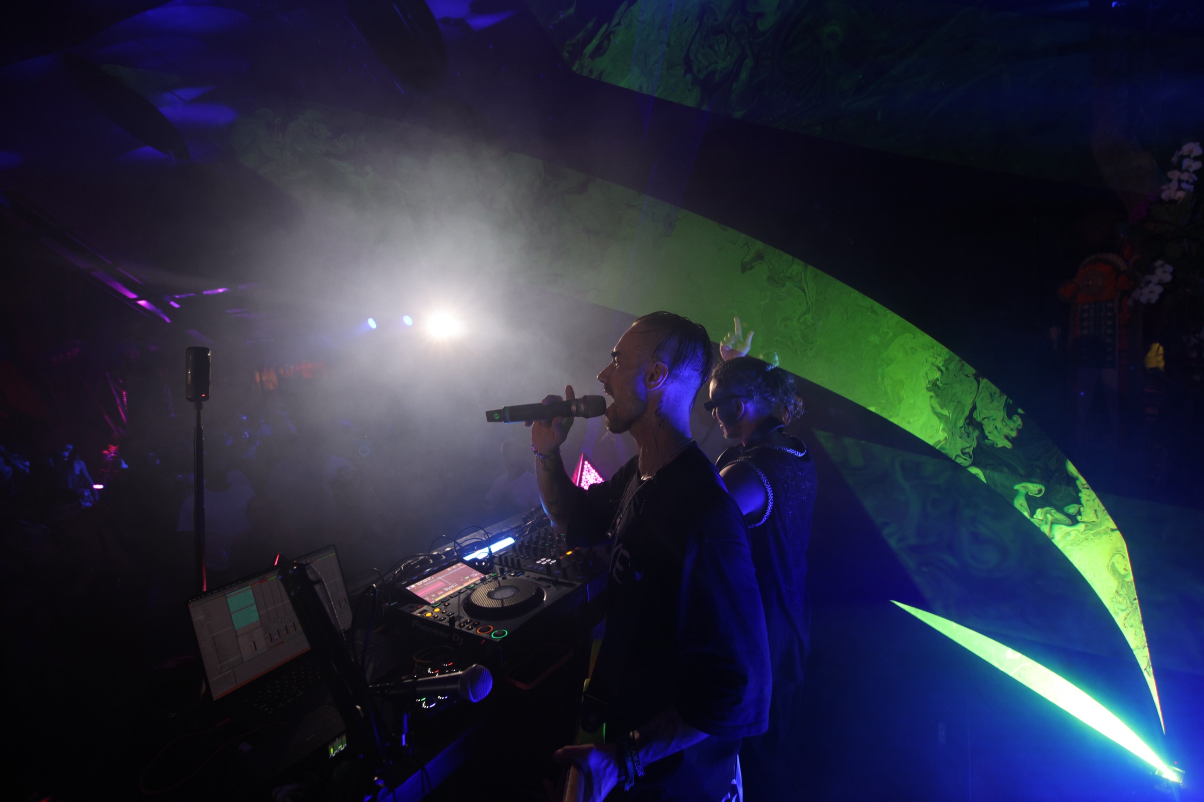 Miguel singing into mic with Shalman at the decks behind, blue purple light at Bali Spirit Festival 2026