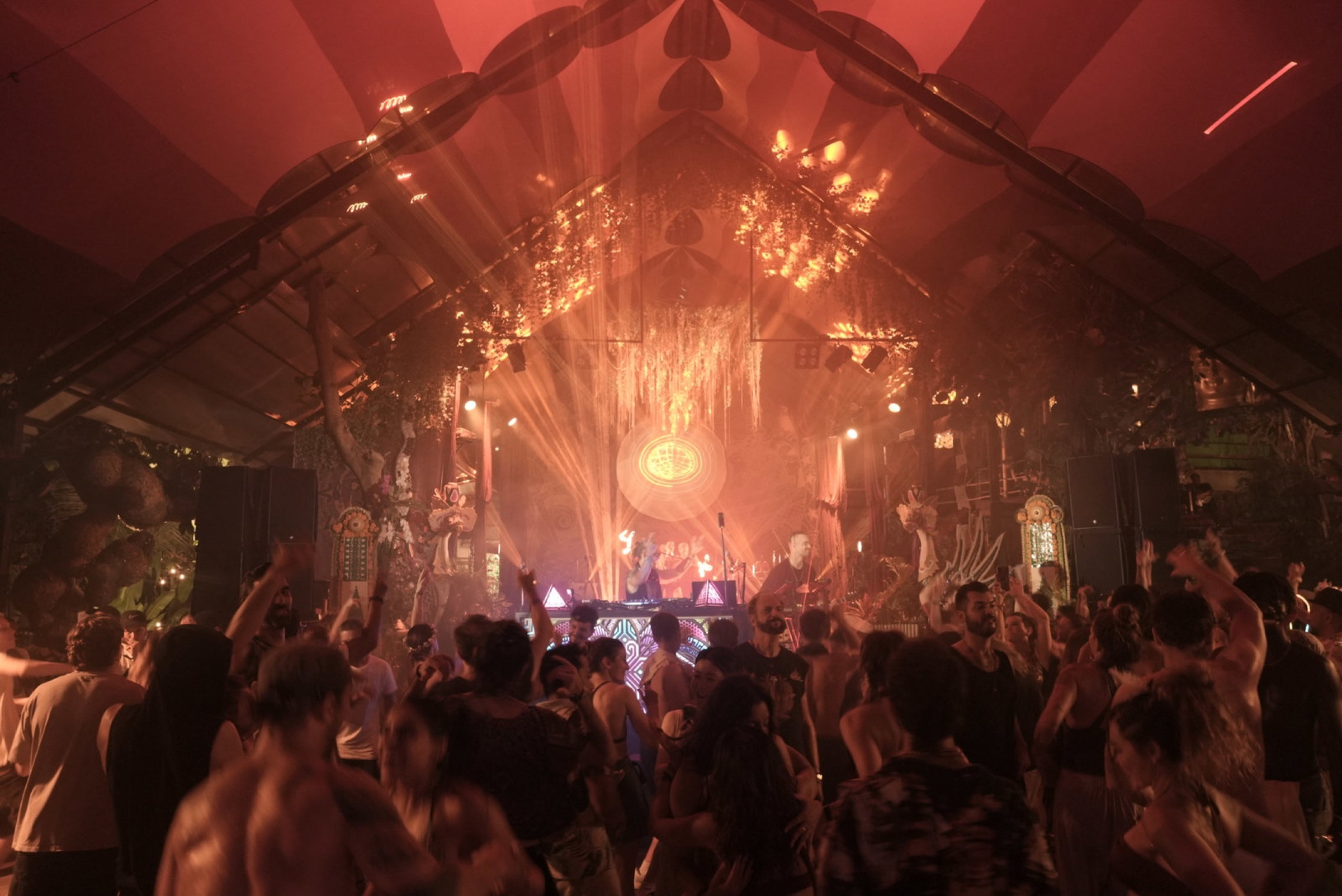 Venue establishing shot at Bali Spirit Festival 2026, mandala backdrop and bamboo ceiling, crowd with hands raised